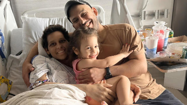 Alexis, Jeff and Ella smile during a photo, all of them in Alexis' hospital bed 