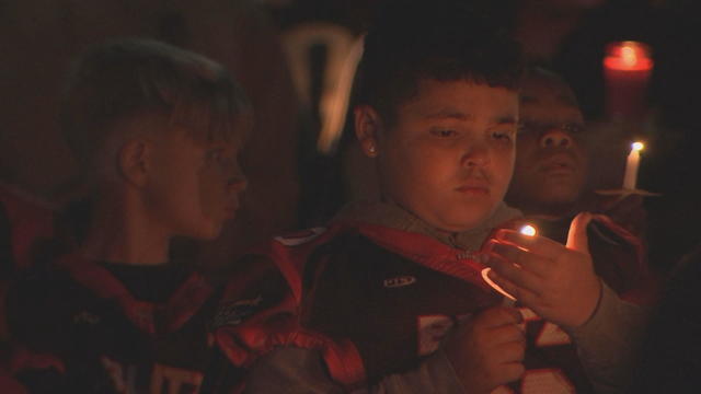 A child holds a hand near a candle during a vigil for the coach 