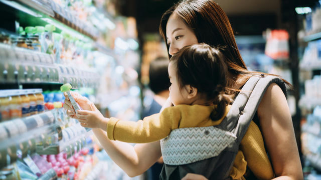 Young Asian mother grocery shopping with little daughter and choosing for organic baby food in the supermarket 