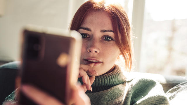 Woman with red hair looking on screen of her mobile phone. 